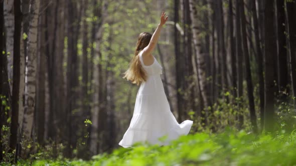 A Young Woman in a Light Flying White Dress is Whirling Around in the Forest