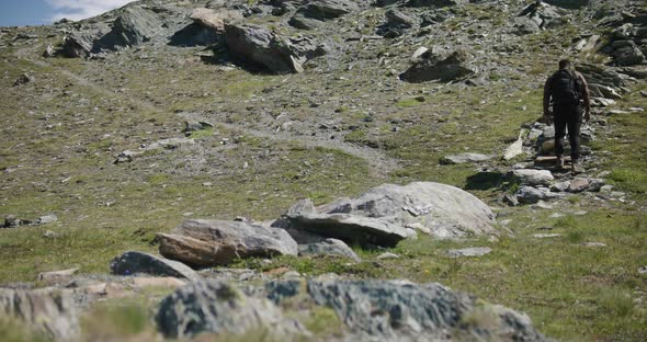 Black male traveler with backpack walking up hill exploring the Matterhorn mountainside in Switzerla