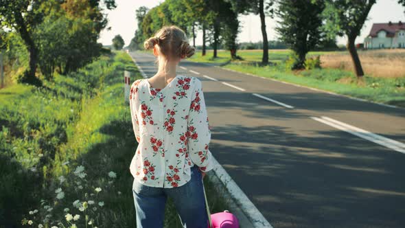 Young Beautiful Woman Hitchhiking Standing on the Road with a Suitcase.