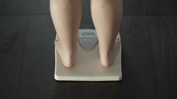 Female measuring weight on bathroom scales, word normal on screen, rear view