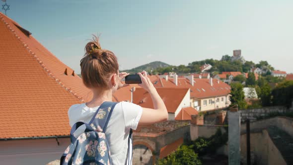 Young Female Tourist Takes Photo By Phone of Red Tile Roofs in Czech Republic