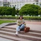 A Girl Sits in the Park on the Stairs Listening to Music and Texting on Her Phone - VideoHive Item for Sale
