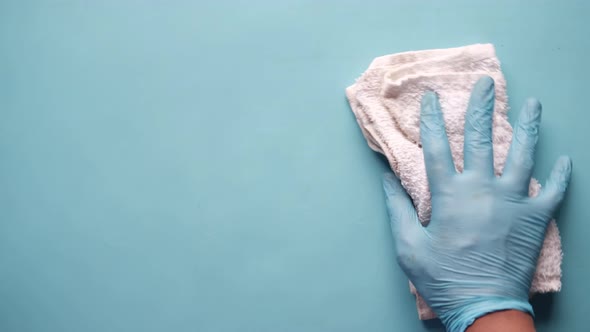 Hand in Blue Rubber Gloves Cleaning Table with Cloth on Blue Background