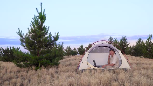 A Man Uses a Laptop for Talking on Video Online in the Tent