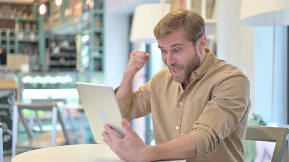 Handsome Man Celebrating Success on Tablet in Cafe 