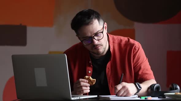 Man working in home office and eating a cookie at table