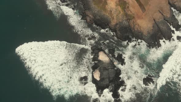 Aerial descending of rocky formations while the waves crash against it on a cloudy day in Pichilemu,