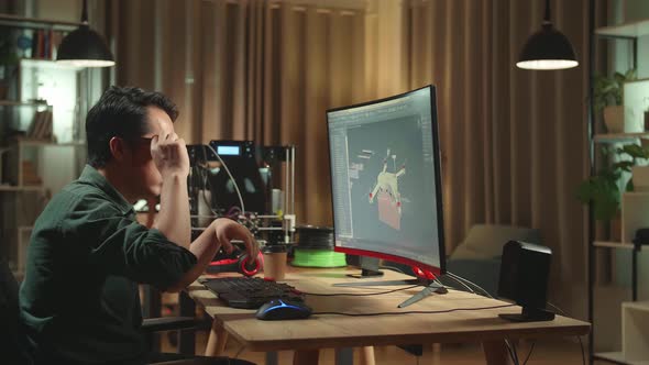 Frustrated Asian Engineer Working On Personal Computer And 3D Printer, Screen Shows 3D Drone