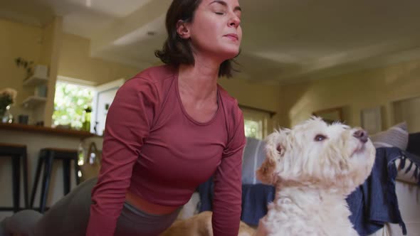 Caucasian woman practicing yoga with her pet dog at home