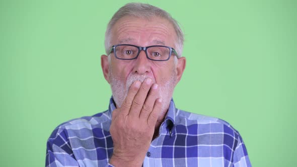 Face of Senior Bearded Hipster Man Looking Shocked and Covering Mouth