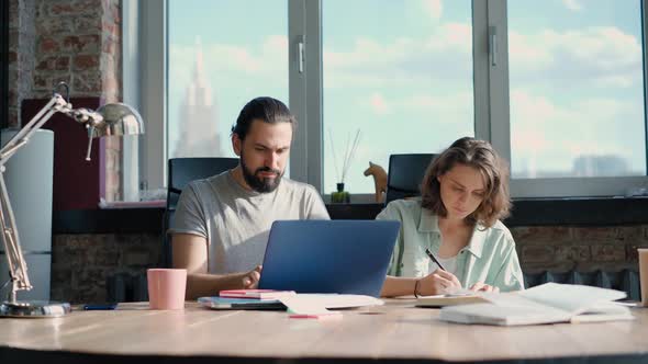 Two Coworkers are Discussing a Project While Sitting in Front of Their Laptops