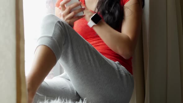 Woman sitting on windowsill and using mobile phone