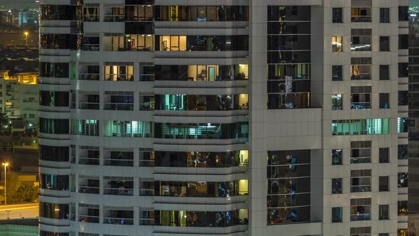 Rows of Glowing Windows with People in Apartment Building at Night