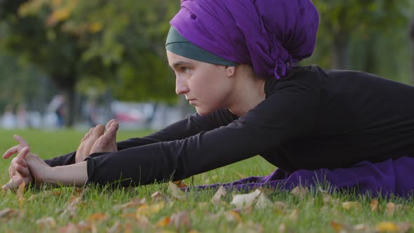 Muslim Woman in Hijab Sits on Green Grass Lawn in Park Bends in Body Doing Fold Female Stretching