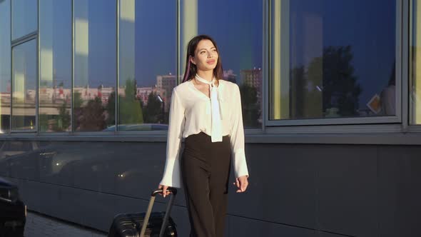 Woman Tourist Smiles Passing Airport Terminal with Suitcase