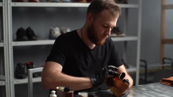 Tracking Shot of Shoemaker in Black Gloves Rubbing Paint on Light Brown Leather Shoes with Fingers