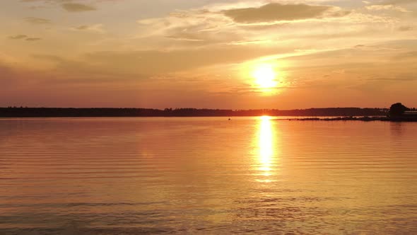 Pier and Boat in the Distance Against the Backdrop of the Setting Sun with Clouds and Water