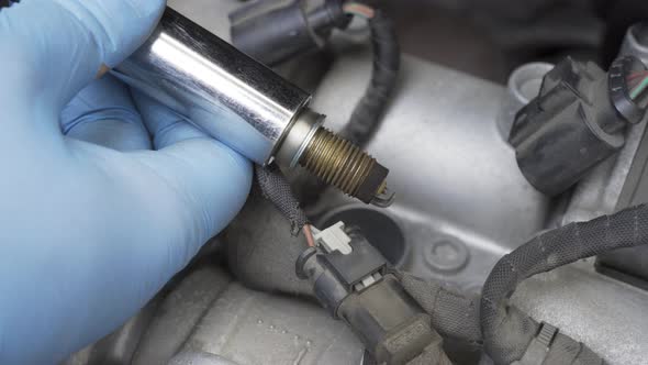 Hands in Protective Gloves Taking Out and Inspecting Spark Plug with Socket Wrench in Car Engine Bay