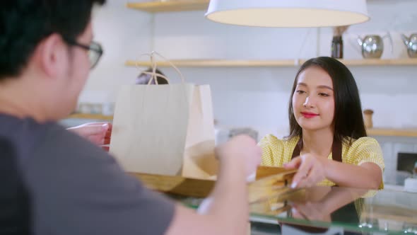 Attractive asian female cafe worker  giving takeaway food bag to customer