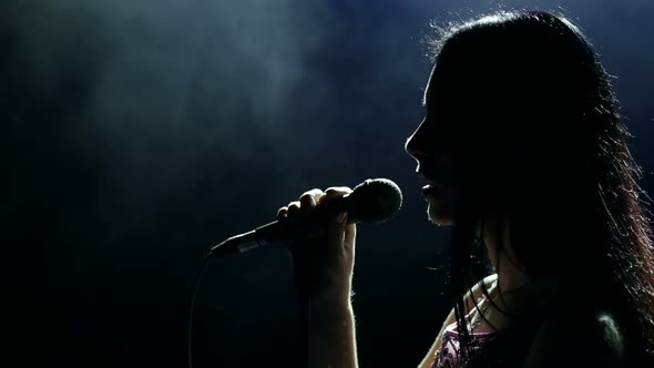Silhouette of Girl Singer with Microphone in Dark