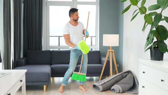 Man Cleaning the House Fooling Around and Having Fun Dancing and Singing with a Broom