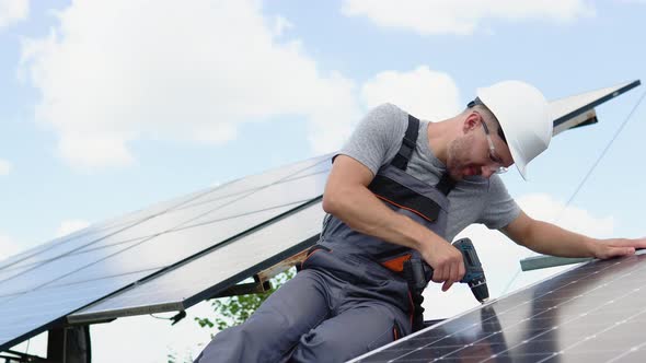 Male Engineer in Protective Helmet Installing Solar Photovoltaic Panel System Using Screwdriver