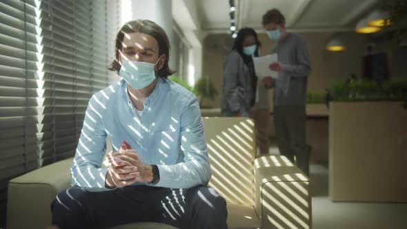 A Serious Businessman is Sitting in Protective Mask and Talking to His Colleague