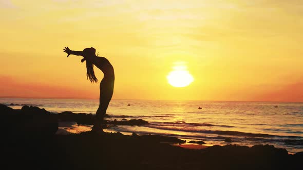 Silhouette of Young Woman Is Doing Yoga Exercises on the Ocean Beach at Sunset.