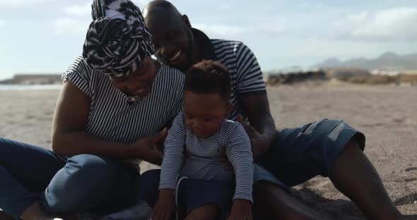 African couple sitting on the beach and having playful time with little son