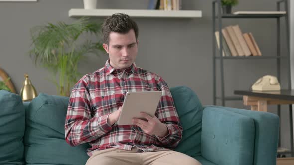 Man Celebrating Success on Tablet on Sofa