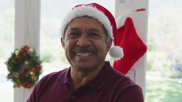 Portrait of cheerful senior man in santa hat at decorated home during christmas