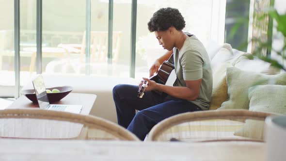 African american man plays guitar and singing, using laptop at home