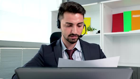 Caucasian young man in suit wearing headphones with mic having video chat at laptop computer