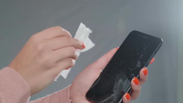 Young Woman Hand Sprays Antiseptic on Black Smartphone