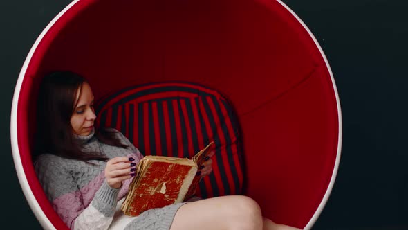 Young Woman Reads Old Book Sitting in Ball Chair