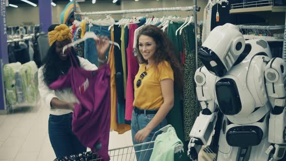 Joyful Ladies Are Picking Clothes with a Cyborg Near Them