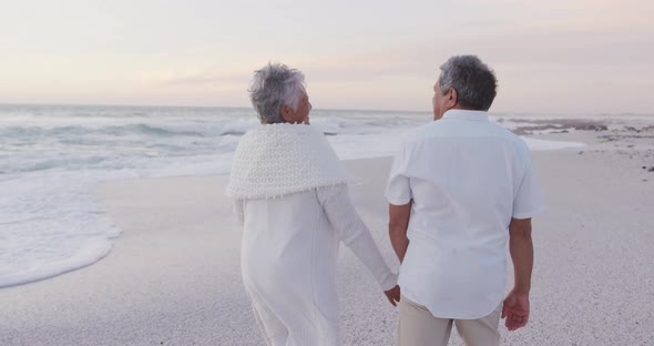 Back view of happy hispanic just married senior couple walking on beach at sunset