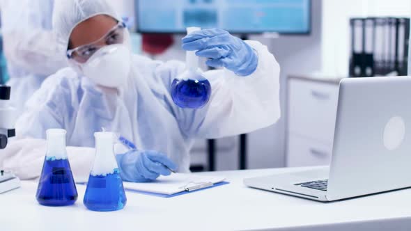 Female Scientist Typing Formula for Different Smoking Blue Fluid in Chemistry Lab