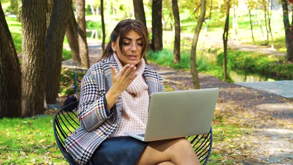 Happy freelancer sitting in garden and having video call on laptop