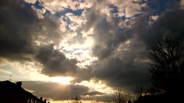 Dramatic Fluffy Clouds, Sunset Timelapse. Pan Right With Silhouette Of Houses And Trees alt