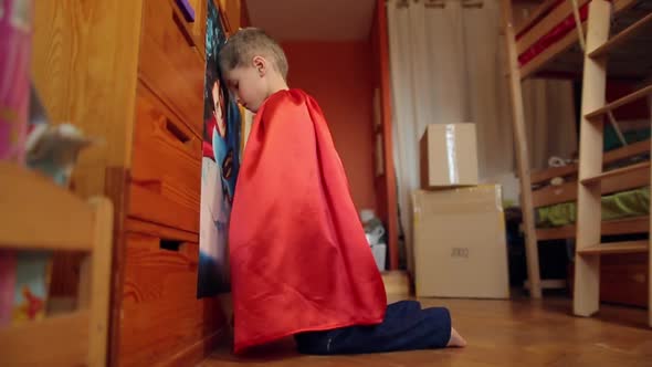 Little Boy In The Suit Of Superman Looks At The Image Of Favorite Character On Poster And Repeats It