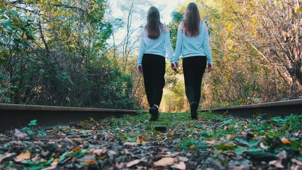 Twins Girls Holding Hands Walking Along Railroad Tracks