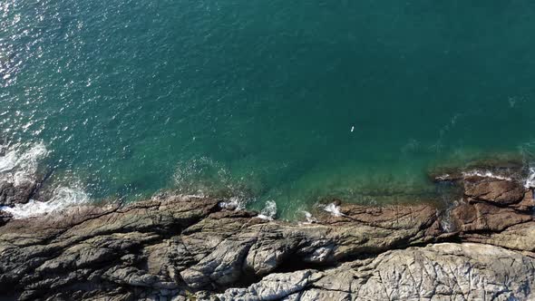 Drone footage of rocky coast and waves bird eye view. Bird flying past camera