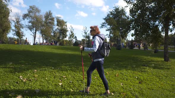 Senior Woman Scandinavian Walking with Tracking Sticks in Park