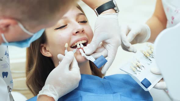 A dentist doctor in medical gloves with an assistant trying on dentures for a young girl.