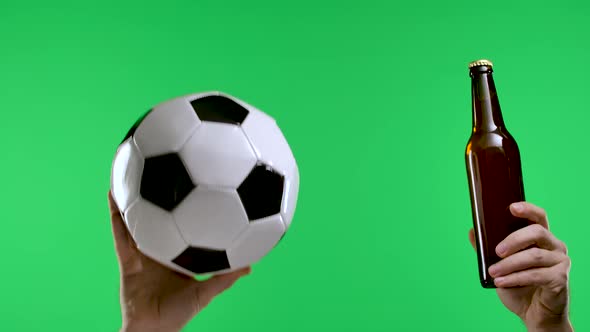 Male Hands Holding Classic Black and White Soccer Ball and Dark Brown Beer Bottle Isolated on Green