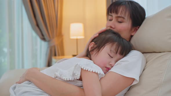 Asian beautiful loving mother hugging sleeping baby girl daughter in her arms with gently at home.