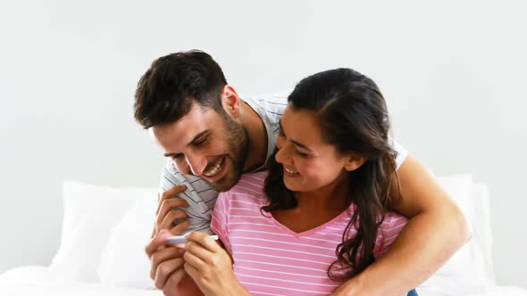 Happy couple looking at pregnancy test on bed in bedroom