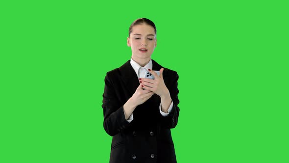 Young Woman in Office Suit Walking Typing Some Text on Her Smartphone and Smiling on a Green Screen