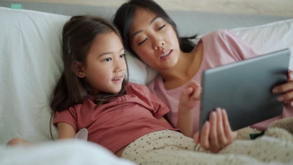 Smiling Asian mother and daughter looking at the tablet